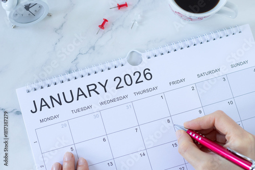 January 2026 calendar with coffee cup, alarm clock and hand holding a pen. New year planning, annual business goal and strategy concept. Top view.