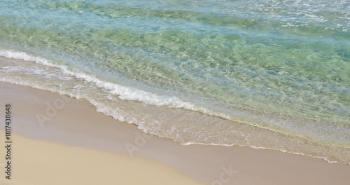 Clear, turquoise ocean waves softly touching the sandy shore. Bright sunlight creates a serene atmosphere, perfect for relaxation and enjoying nature.