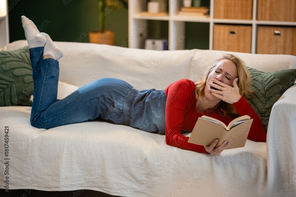 Fototapeta premium Woman yawning while reading book on sofa