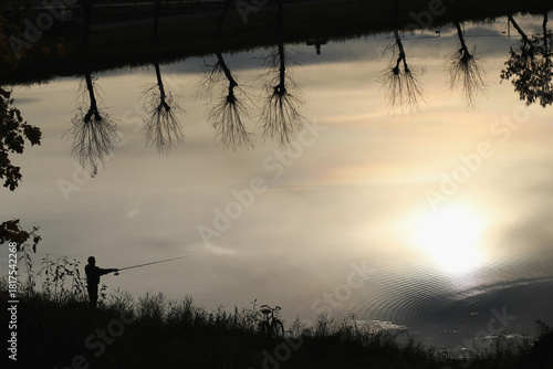 Silhouette of a fisherman at sunset on a calm lake with reflections