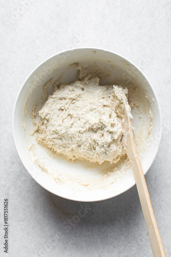Overhead view of artisan bread dough being mixed in a white bowl, process of making bread dough
