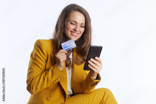 A confident businesswoman in a bright yellow suit smiles while holding a credit card and smartphone, embodying modern online finance and secure digital transactions.