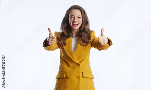 A smiling businesswoman in mustard yellow blazer gives double thumbs-up gesture, radiating positivity and approval. Against plain white background, she embodies confidence, success and agreement