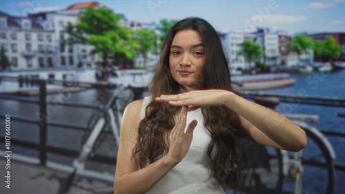 Woman in white sleeveless top making time out gesture with crossed hands on street; calm introspection.