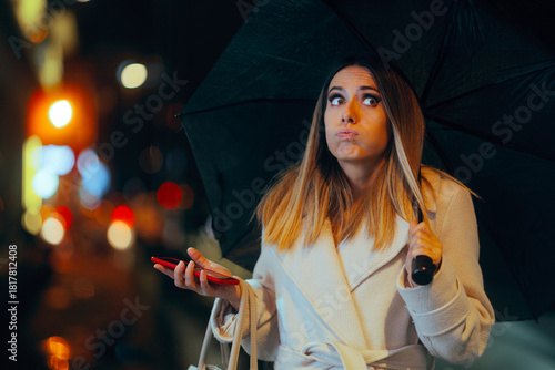 Puzzled Lady Holding her Phone and an Umbrella. Pedestrian trying to get a taxi on a gloomy weather using an app