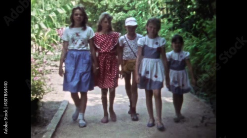 Happy children group walking along path in lush green park during sunny summer holiday. Carefree childhood. Nostalgia child friendship. Kids together in old film. Archival retro 1960s. Vintage archive