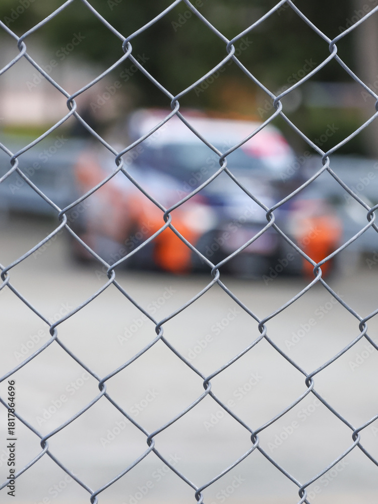 Fototapeta premium Chain link fence barrier on motorsport track, watching race car at high speed. blur of competition creates feeling of intense anticipation from distance