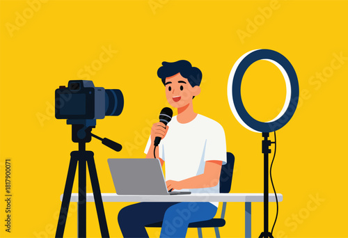 A smiling man in a white tee, speaks into a mic while using a laptop. Camera and ring light setup