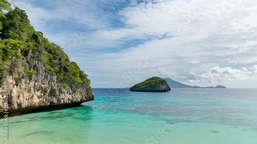 4k, Scenic view of a rocky promontory extending into turquoise water, with an island visible in the distance under a partly cloudy sky, taken with wide-angle lens and