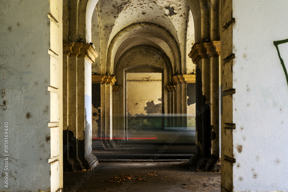 Fototapeta premium Speeding vehicles leave streaks of motion inside an abandoned arched passageway, highlighting the clash of modern movement with decayed architectural details.