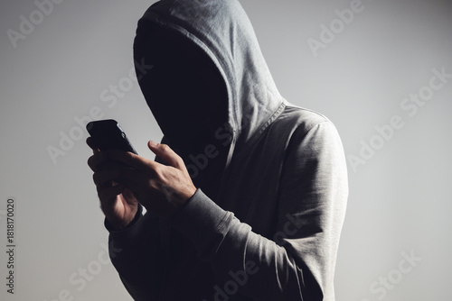 Canvas Print Man in hoodie using smartphone in dark shadow, face hidden in black, concept of anonymity, secrecy, cybercrime, or privacy