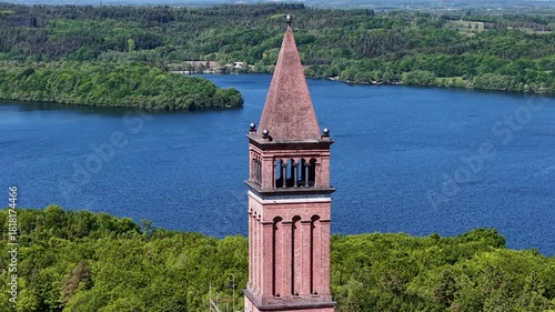 Dramatic aerial footage of the historic Himmelbjerget tower rising above a deep blue lake and green forests in Denmark.