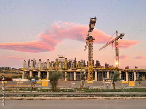 A modern construction site with tall cranes at sunset. Industrial building, urban development, architecture, and progress. City street, construction in progress. Athens, Greece.