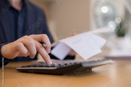 Close-up of businessman using calculator while holding financial document. Concept of accounting, finance report, budget calculation, expense tracking business data management.