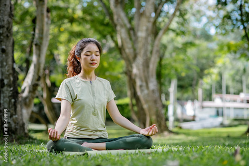Wallpaper Mural A young Asian woman meditating peacefully for a warm-up before doing yoga on the grass, practising in a green outdoor park with morning sunlight, showing a healthy, calm, and relaxed lifestyle Torontodigital.ca