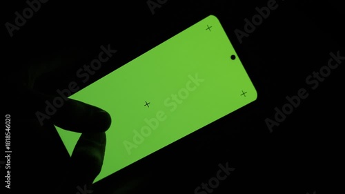 Close-up nighttime shot of a large-screen smartphone held in one hand while fingers type on the display. The glowing screen shows active mobile trading, financial analysis, or investment activity.