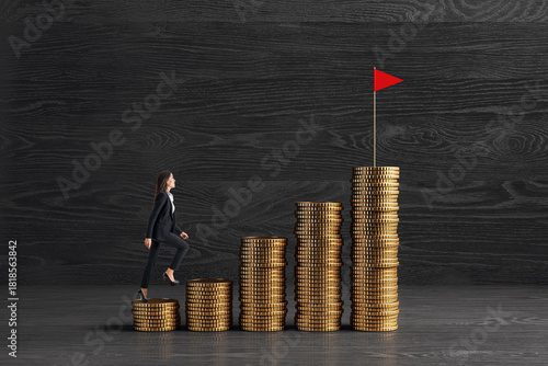 Businesswoman climbing coin stacks like stairs toward red flag symbolizing financial goal, growth, and achievement on dark wooden background.