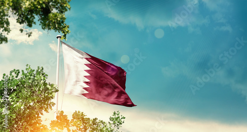 Qatar national flag waving in the sky behind the tree. The flag blowing with beautiful sunlight. Qatar national flag for independence day.
