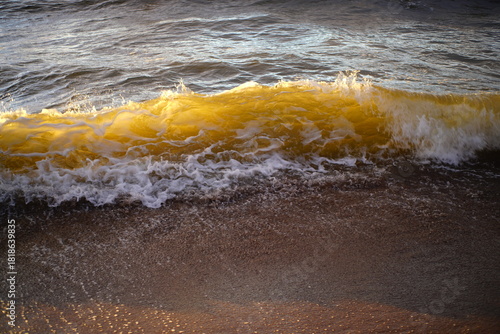 Fototapeta Naklejka Na Ścianę i Meble -  The sunset time golden hour walk to the Baltic sea in Lithuania, Europe, evening view of the yellow and red clouds, ocean waves in storm, girl walking in sport shoes, grey sand grains travel lifestyle