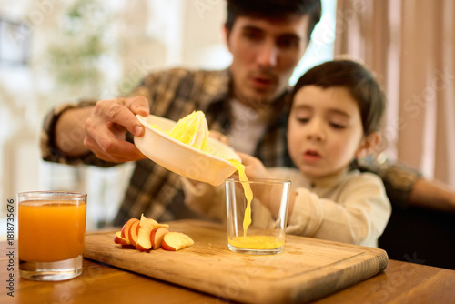 Fresh squeezed citrus juice poured by father and son into glass with warm kitchen mood. Concept of beverage visuals, family lifestyle, healthy habits and emotional storytelling.