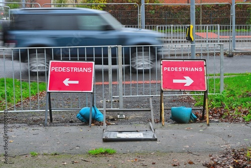 Fotografie Confusing Pedestrian Signs with Barricades on Wet Urban Roadside