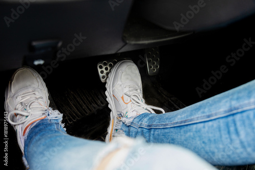 Feet in white sneakerson car brake pedal close-up