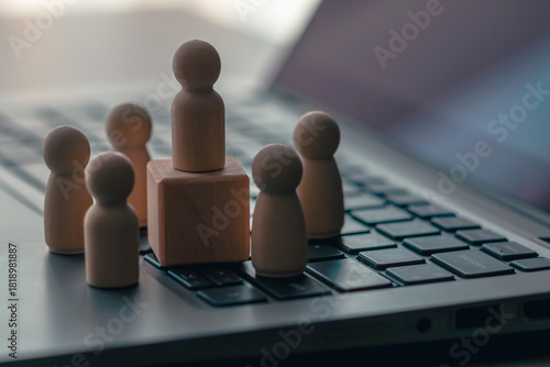 Wooden pawns on a laptop. One stands tall, symbolizing leadership, thinking different, and achieving success