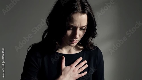 Emotional distress portrayed: A woman experiencing grief, heartbreak, or pain, touching her chest in a somber, dimly lit setting, suggesting