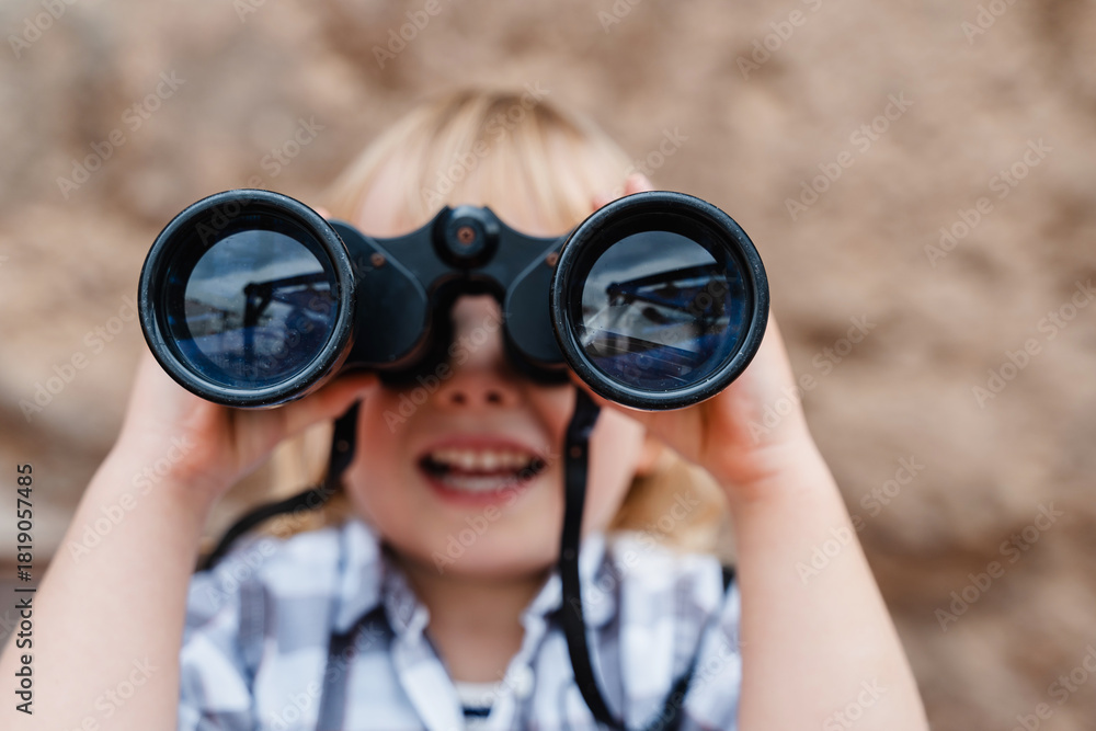 Obraz premium Portrait of playful child using binoculars outdoors. Little girl watching binoculars. Concept of childhood, adventure, imagination and discovery.