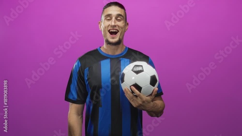 Man holding soccer ball with hand, smiling in studio wearing blue striped jersey; joyful celebration.