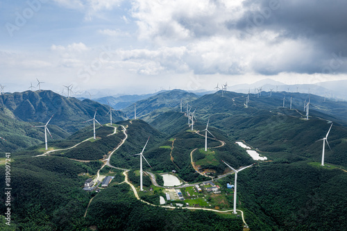 Aerial view of wind farm and winding roads on green mountains in rural area.