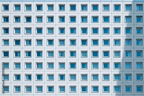 Close Up of a Modern Building Facade with Numerous Square Windows and Blue Curtains, Showing a Repetitive Geometric Pattern