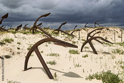 Rusting iron anchors arranged in sand dunes at Praia do Barril, Tavira, Portugal, memorial to tuna fishing heritage,
