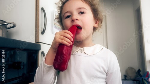Little girl examining and eating red pepper in home kitchen