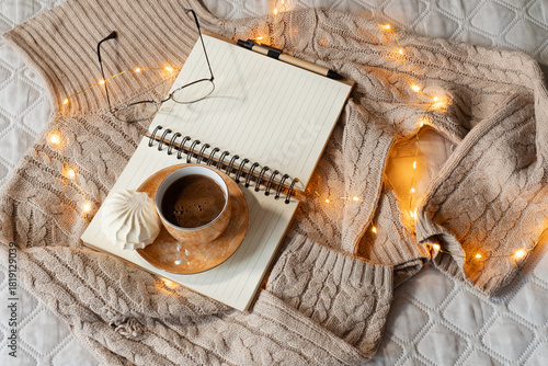 Cozy home atmosphere. Warm beige sweater, mug with coffee, book and eyeglasses on gray bed in bedroom. Hygge concept. Horizontal banner, web site