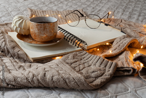 Cozy home atmosphere. Warm beige sweater, mug with coffee, book and eyeglasses on gray bed in bedroom. Hygge concept. Horizontal banner, web site