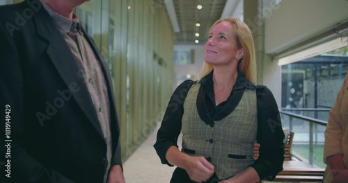 Confident female team member leading conversation with colleagues in modern office hallway, diverse group engaged in professional workplace discussion