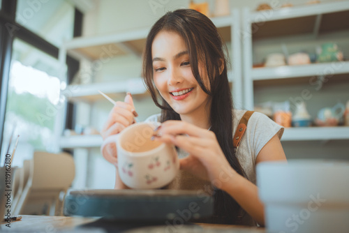 Asian woman painting ceramic art and pottery designs in her studio – happy artisan potter sitting with handmade tools, enjoying sculpting process and creative small business lifestyle