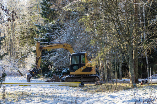 An excavator stands idle on a snow-covered construction site, surrounded by winter conditions and a quiet, frozen landscape