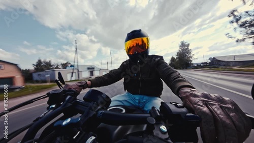 Motorcyclist riding a bike on a forest road captured by a selfie camera. Rider wearing a helmet with a gold visor and a bomber jacket driving fast.