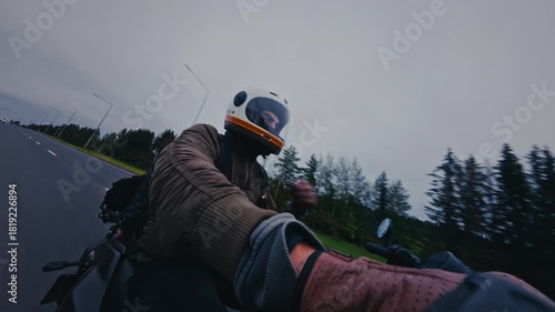 Motorcyclist riding a bike on a forest road captured by a selfie camera. Rider wearing a helmet with a gold visor and a bomber jacket driving fast.