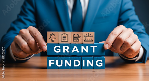 Businessman holding blocks spelling out grant funding with icons representing business