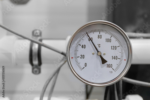 A round analog thermometer on industrial equipment shows a temperature above 60 degrees Celsius