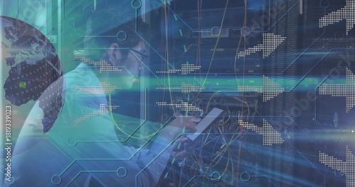 Working Korean technician adjusting cables at server racks, holding tablet in white shirt, glasses
