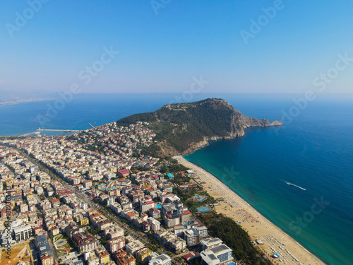 Fototapeta Naklejka Na Ścianę i Meble -  Wide aerial panorama of the dense urban area of Alanya, the mountainous peninsula, and the long stretch of beach meeting the turquoise Mediterranean Sea