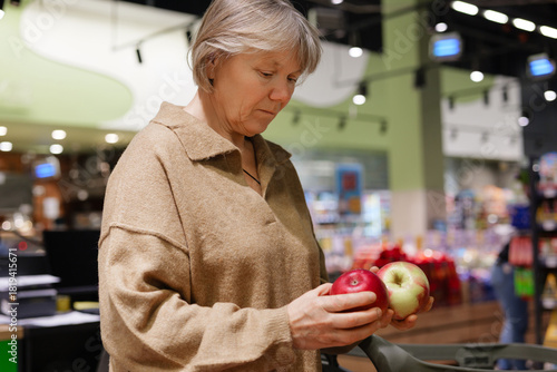 Canvas Print A woman examines two apples in a grocery store, deciding between a red and a green one