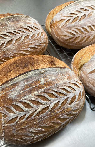 Close up of homemade artisan sourdough bread crust showing beautiful scoring pattern, resting on a cooling rack after baking.