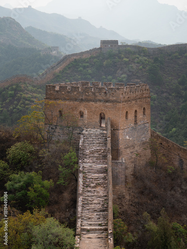 View of ancient stone steps ascend towards a formidable watchtower along the Great Wall, nestled amidst misty mountains, Beijing, Beijing, China.