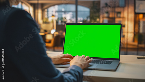 Over the shoulder shot of a business woman working in office interior on pc on desk, looking at green screen. Office person using laptop computer with laptop green screen