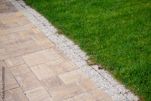 Paved walkway with gravel edge bordering lush green lawn. Landscape design, property maintenance, hardscape transition. Real photo.